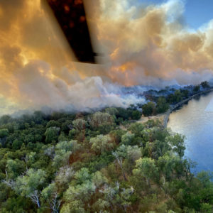 Fire in wooded area as seen from helicopter with one blade in the frame