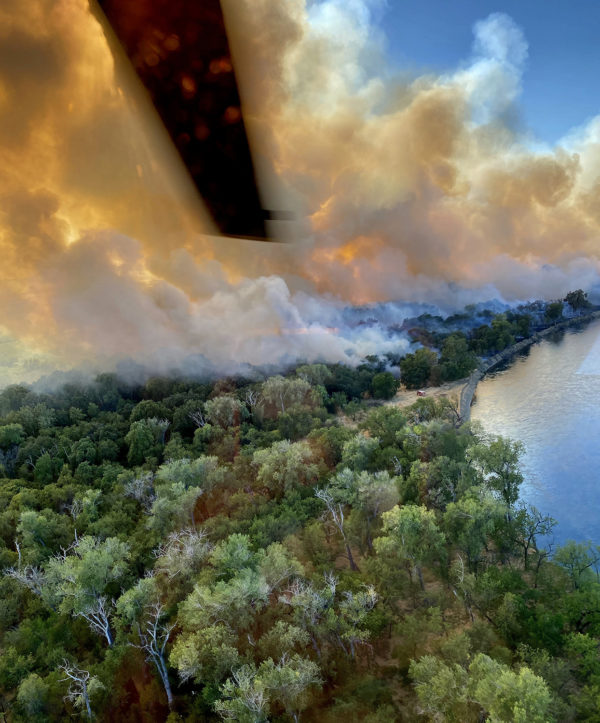 Fire in wooded area as seen from helicopter with one blade in the frame