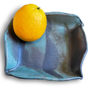 Hand-built pottery platter with blue glazes and an orange on top